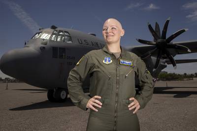 A smiling Maj. Sarah Spy poses with her hands on her hips while standing in front of a C-130 Hercules on the tarmac.
