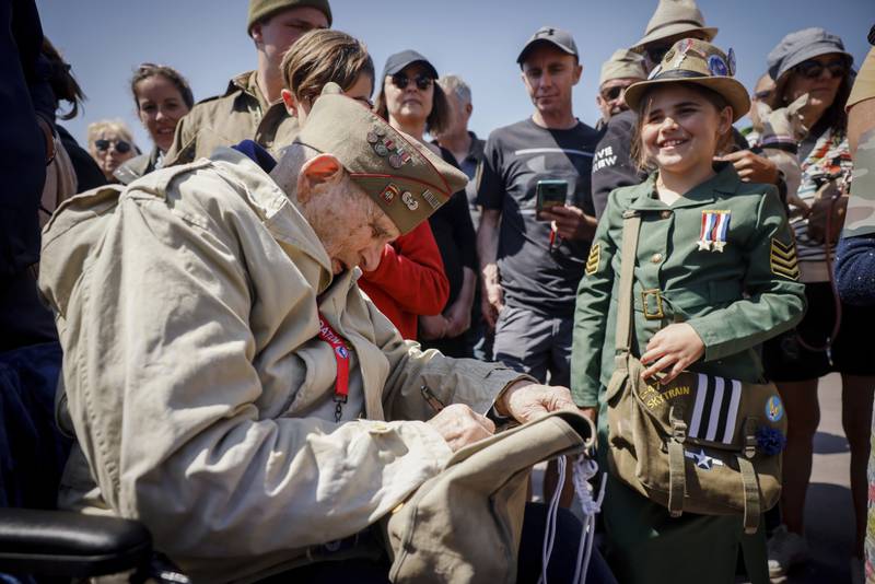 A U.S. veteran signs the bag of a World War II enthusiast during a gathering in preparation of the 79th D-Day anniversary in Sainte-Mere-Eglise Normandy, France, Sunday, June 4, 2023.