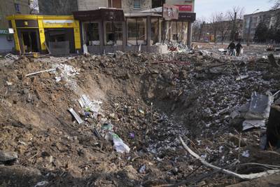 People walk past a crater from an explosion on Mira Avenue (Avenue of Peace) in Mariupol, Ukraine, Sunday, March 13, 2022. The surrounded southern city of Mariupol, where the Russian war on Ukraine has produced some of the greatest human suffering, remained cut off despite earlier talks on creating aid or evacuation convoys. (AP Photo/Evgeniy Maloletka)