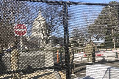Members of the National Guard stand inside anti-scaling fencing that surrounds the Capitol, Sunday, Jan. 10, 2021, in Washington.