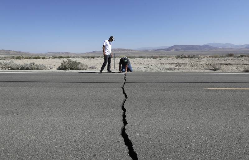 Ron Mikulaco, right, and his nephew, Brad Fernandez, examine a crack caused by an earthquake on Highway 178, Saturday, July 6, 2019, outside of Ridgecrest, Calif.