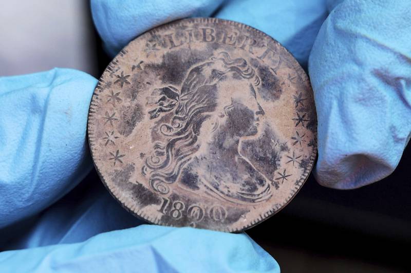 This photo, provided by the U.S. Military Academy at West Point, Aug. 30, 2023, shows West Point archeologist Paul Hudson display an 1800 Draped Bust Dollar, one of the coins found in the lead box believed to have been placed in the base of a monument by cadets almost two centuries ago, in West Point, NY.