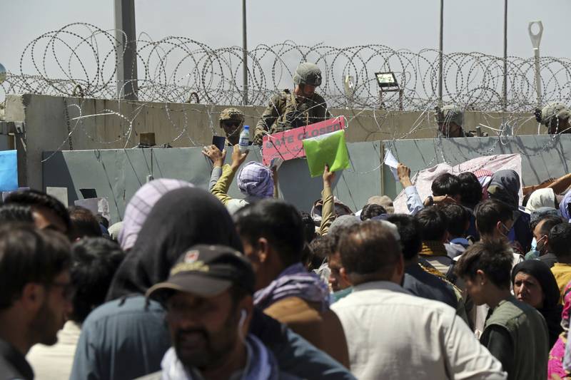 A U.S. soldier holds a sign indicating a gate is closed as hundreds of people gather some holding documents, near an evacuation control checkpoint on the perimeter of the Hamid Karzai International Airport, in Kabul, Afghanistan, Aug. 26, 2021. (Wali Sabawoon/AP)
