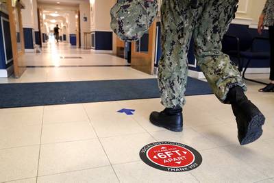 A social distancing sign is seen on the floor as a midshipman walks to class at Luce Hall at the U.S. Naval Academy, Monday, Aug. 24, 2020, in Annapolis, Md.